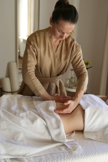 Eine Therapeutin führt eine Massage an einer liegenden Person durch.