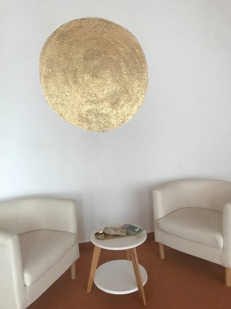 Zwei weiße Sessel mit einem kleinen Tisch und einer goldenen Wanddekoration.