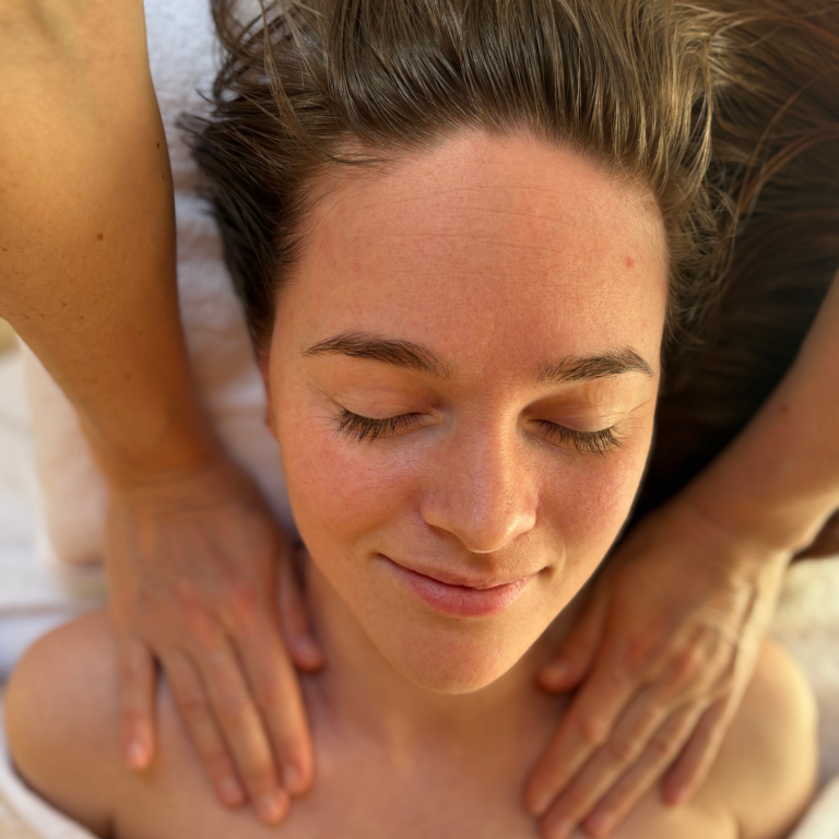 Frau erhält eine entspannende Massage, sie lächelt und hat geschlossene Augen.